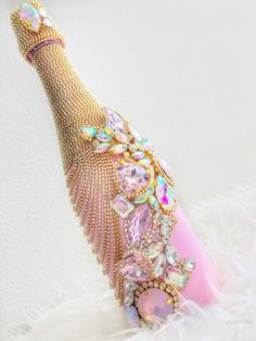 a pink bottle with lots of jewels on it sitting on top of a white feather