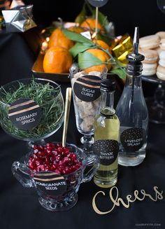 a table topped with bottles and bowls filled with food next to desserts on top of a black cloth covered table