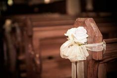 a white rose sitting on the back of a wooden pew at a church wedding ceremony