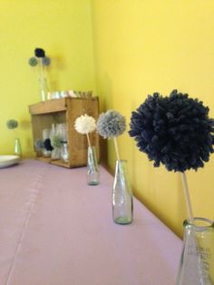 three vases with flowers in them sitting on a table next to a yellow wall