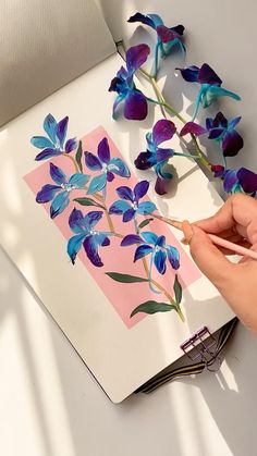 a person is painting flowers with watercolors on a piece of paper that they are holding in their hands