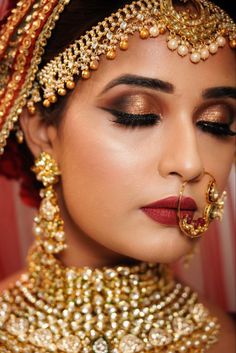 a woman wearing gold and red makeup looks down at her face with the nose ring in front of her