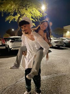 a man carrying a woman on his back in the middle of a parking lot at night