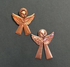 two gold angel brooches with skulls on them sitting next to each other in front of a gray background