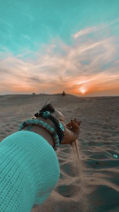 a person is holding sand in their hand while standing on the beach at sunset or sunrise