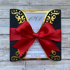 a black and gold wedding card with a red bow on it's front pocket