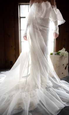 a woman in a white wedding dress is standing by a window with her hands on her hips