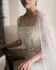 a woman in a wedding dress sitting on a chair with her hand on the arm