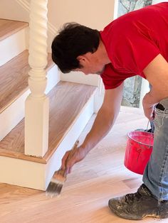 a man in red shirt and jeans painting stairs with white paint on wooden flooring