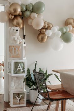 some balloons are hanging on the wall above a chair and table with a teddy bear