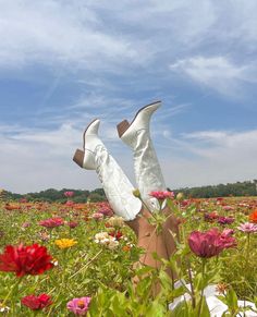 a woman's legs in white high heeled shoes laying in a field of flowers