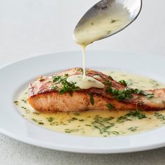 a spoon drizzling sauce onto a piece of salmon on a white plate