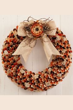 a wreath made out of pine cones is hanging on the wall with an orange flower