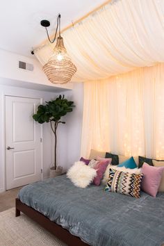 a bed sitting under a white curtain next to a potted plant in a bedroom