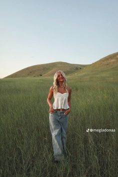 a woman standing in tall grass with her hands on her hips