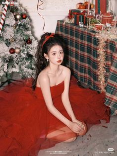 a woman in a red dress sitting next to a christmas tree