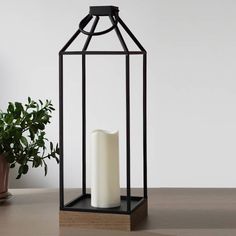 a white candle in a black cage next to a potted plant on a table