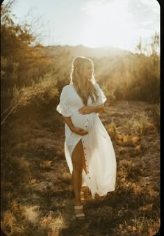 a pregnant woman walking through the desert in her white dress, with sunbeams behind her