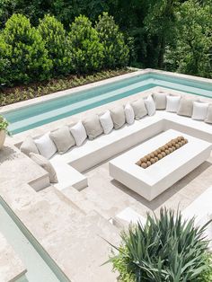 an outdoor seating area next to a swimming pool with plants and trees in the background