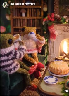 two stuffed animals sitting in front of a cake on a table next to a fireplace