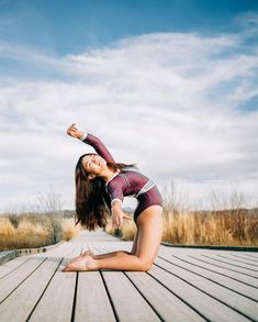 a woman is doing yoga on a wooden deck in front of some tall grass and blue sky