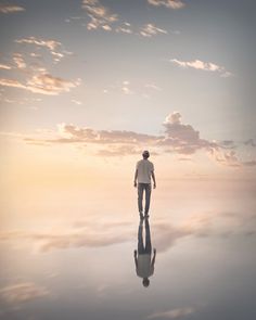 a man walking across a large body of water with the sun setting in the background