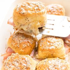 ham and cheese sliders being lifted with a fork from a casserole dish