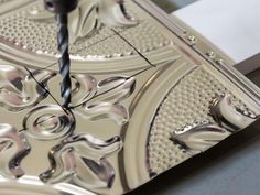 a drill is being used to make decorative designs on a piece of silver metal ornament