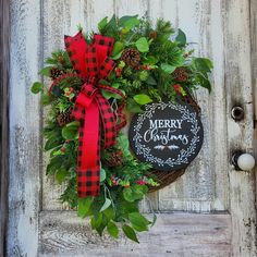 a christmas wreath hanging on a door with a chalkboard saying merry christmas and pine cones