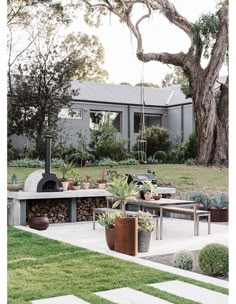 an outdoor patio with potted plants and a pizza oven in the center surrounded by trees