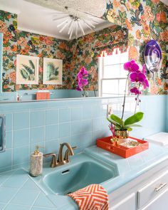 a blue sink in a bathroom with flowers on the wall and pictures hanging above it