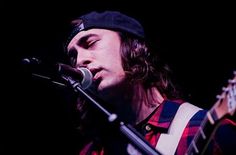 a man with long hair and a hat on singing into a microphone while holding a guitar