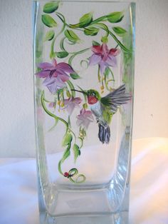 a glass vase with flowers painted on the side and hummingbirds in flight above it