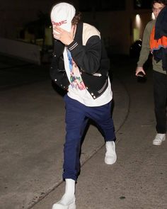 two people walking down the street at night, one is wearing a hat and holding a cell phone to his ear