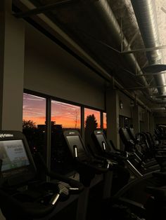 there are many treadmills in the gym with sunset out the window behind them