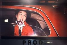 a woman sitting in the back seat of a red car with an advertisement on it's side window