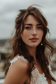 a woman with long brown hair wearing a white dress and pearls on her head is looking at the camera