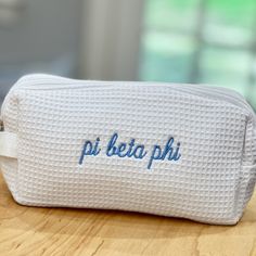 a white bag with the word pi beta phi embroidered on it sitting on top of a wooden table