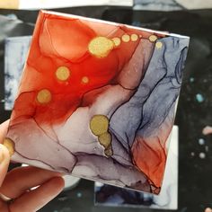 a hand holding a square glass tile with gold dots on it