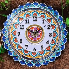 a clock that is sitting on the ground next to some leaves and grass, with an image of a butterfly in the center