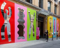 people are standing in front of colorful art on the side of a building that has been painted pink, green, yellow and red