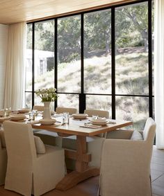 a dining room table set with place settings in front of large windows overlooking the woods