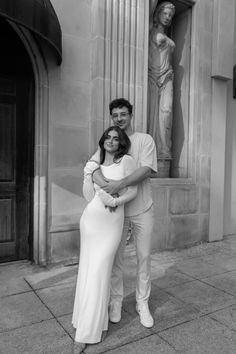 a man and woman standing next to each other in front of a statue on the side of a building