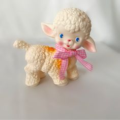 a small white sheep figurine with a pink bow around its neck on a white background