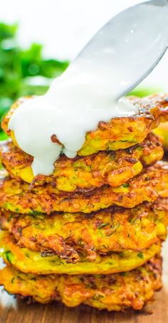 a stack of zucchini fritters being drizzled with white sauce