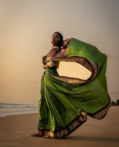 a woman standing on top of a beach next to the ocean holding a green sari