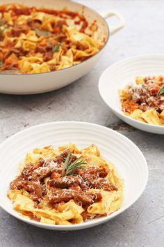 three plates of pasta with meat and sauce in them on a counter top next to a pot