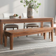 a wooden table with white chairs and a bench in front of it on a rug