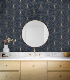 a bathroom vanity with an oval mirror and gold accents on the wall above it, along with two vases filled with flowers