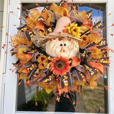 a wreath that is hanging on the front door with an orange and yellow fall decoration